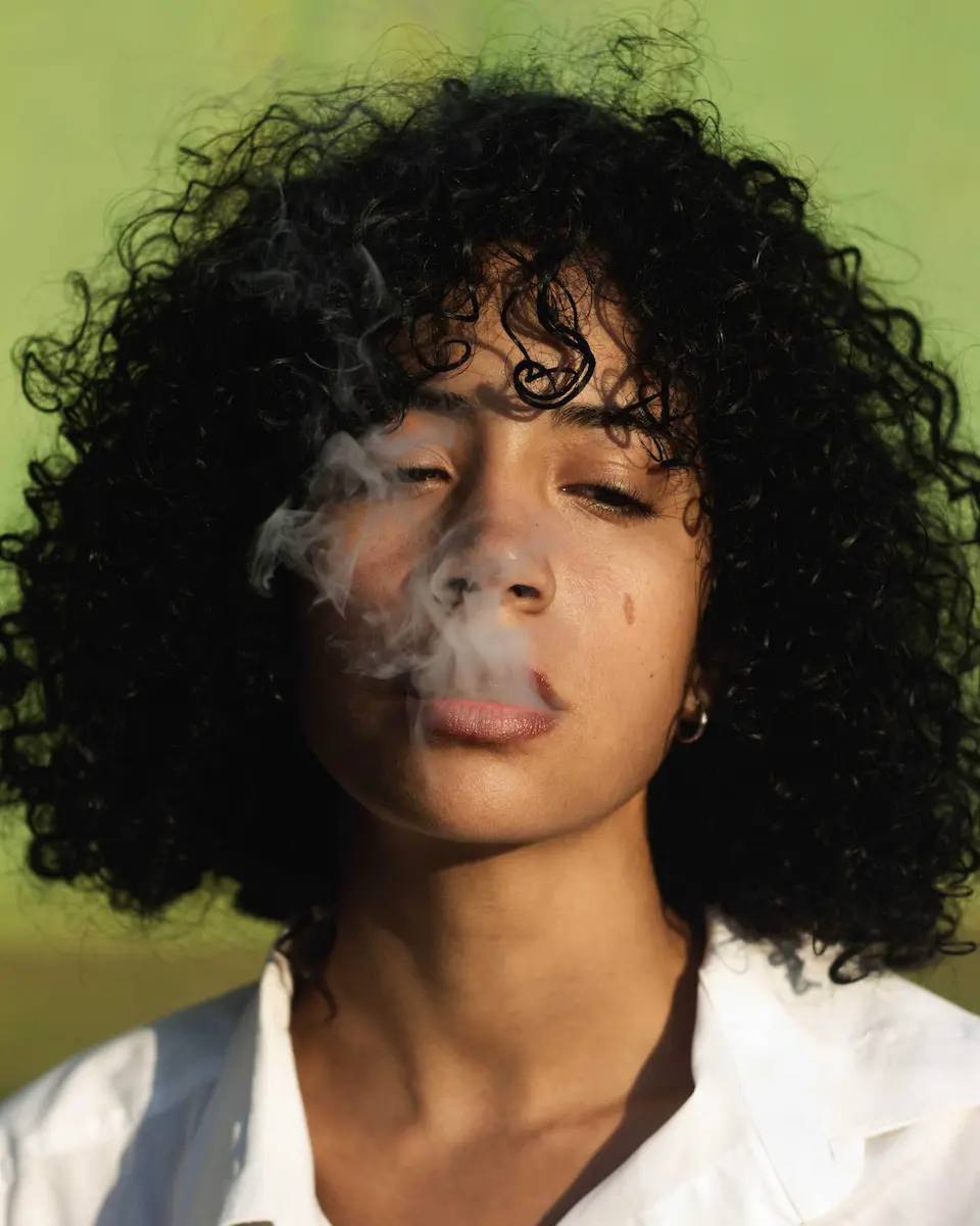 chica mulata de rizos soltando humo por la boca